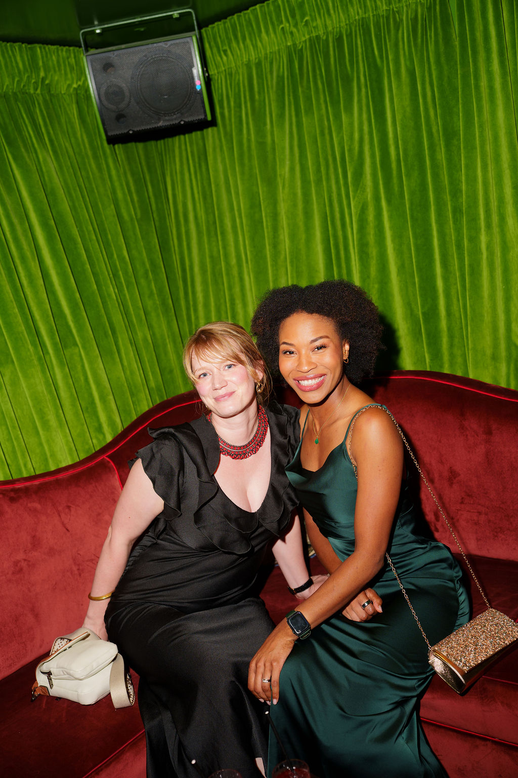 Two elegantly dressed women seated together on a red velvet sofa