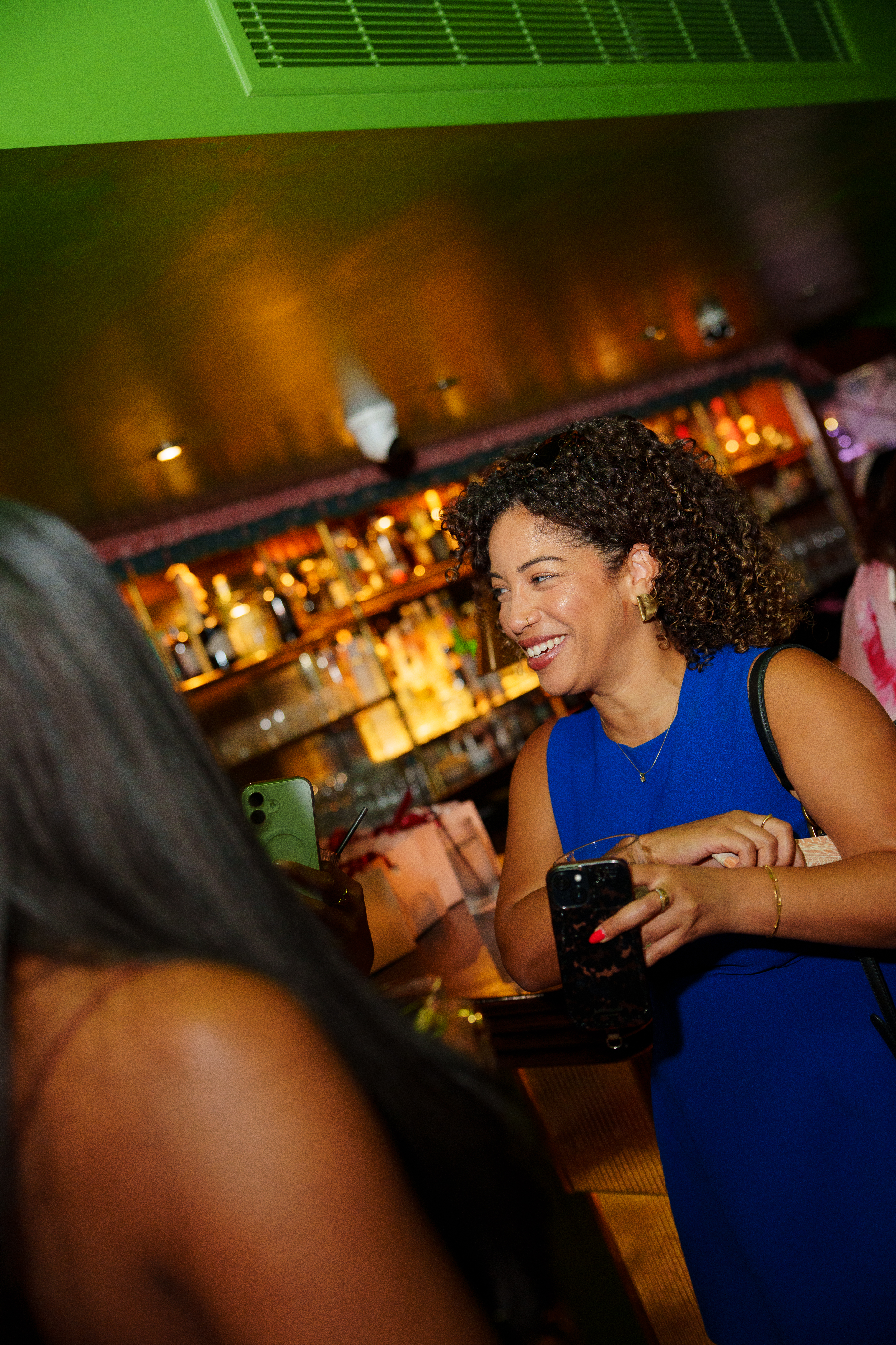 A woman in a vivid blue dress laughing during a conversation at the bar