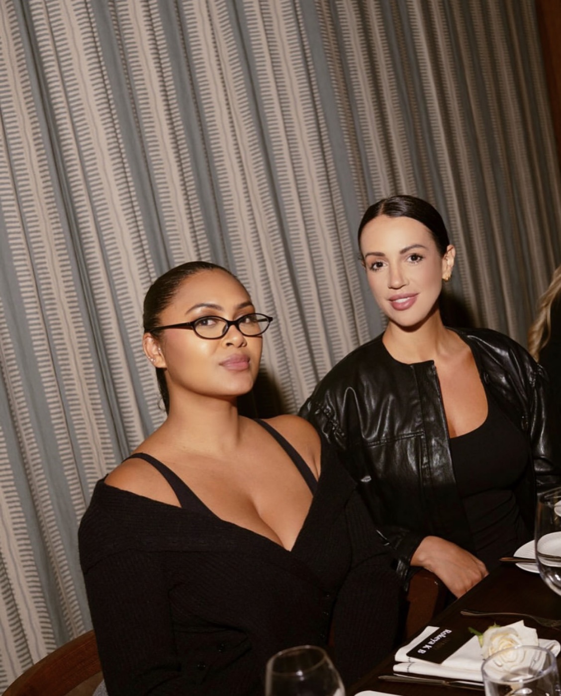 Two elegantly dressed women seated together at an intimate dinner