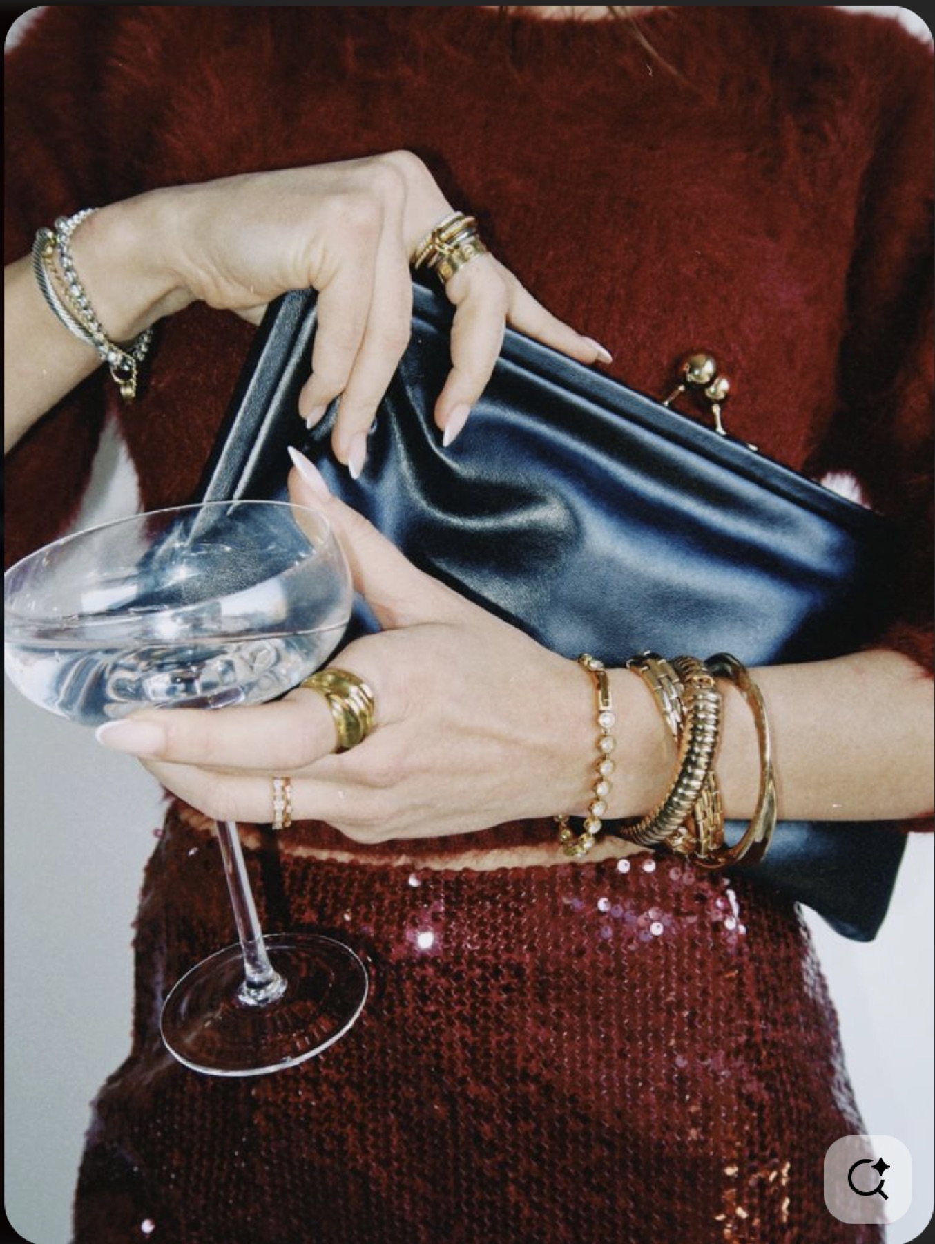 A guest holding an evening bag and cocktail, her hands layered with jewellery