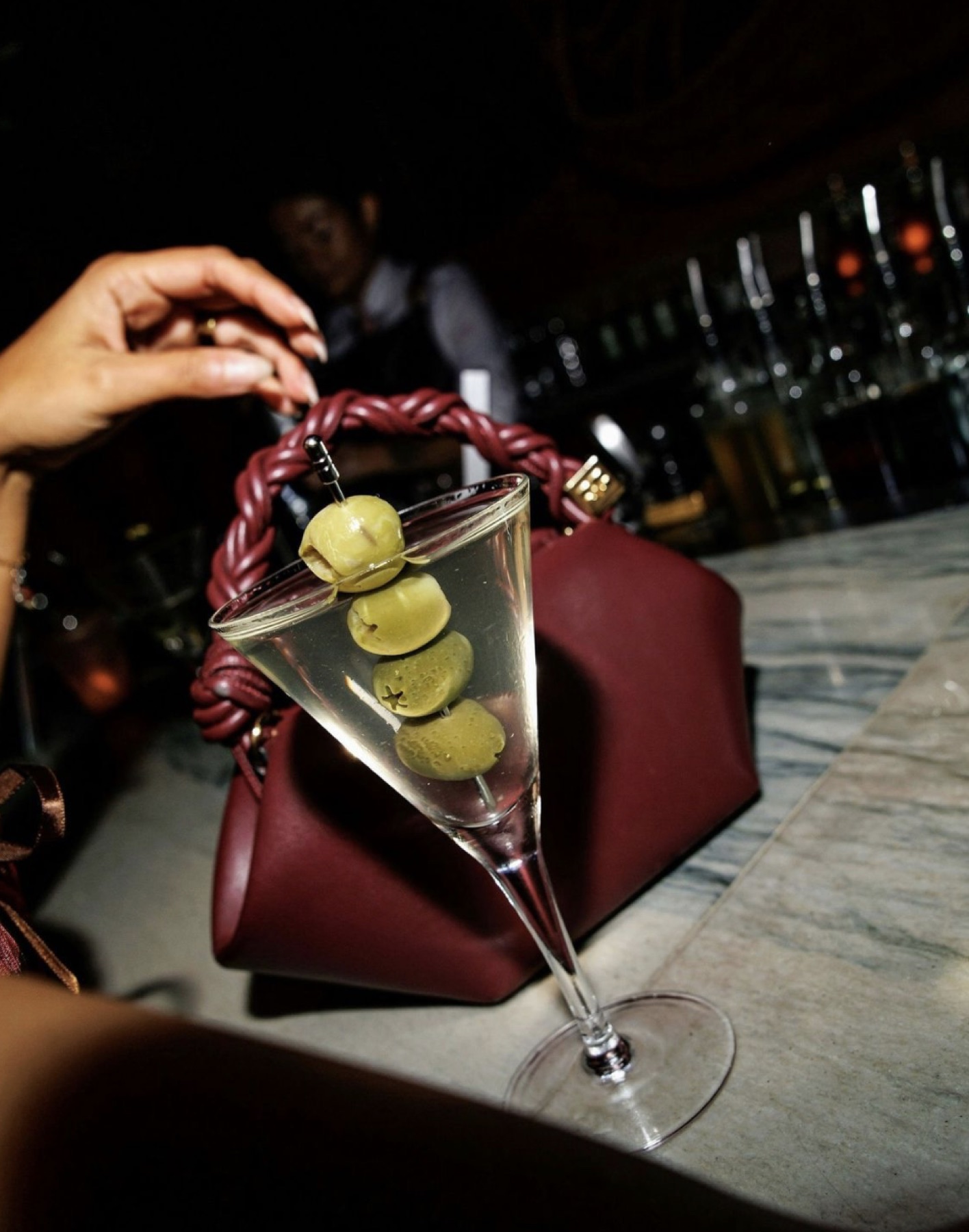 A martini with olives beside a sculptural burgundy handbag
