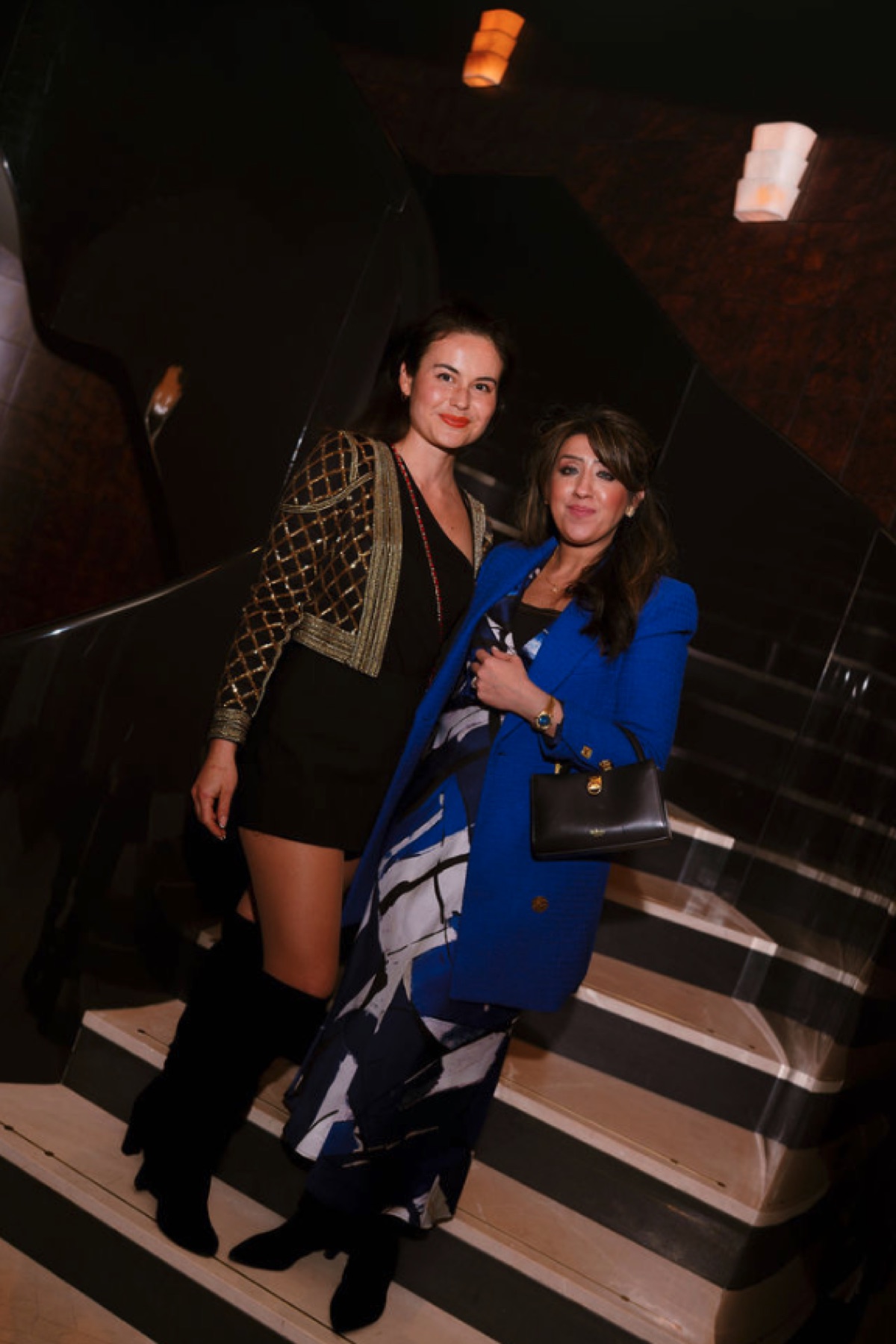 Two elegantly dressed women standing together on a staircase